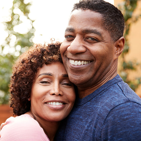 A middle-aged couple embraces and smiles outside.